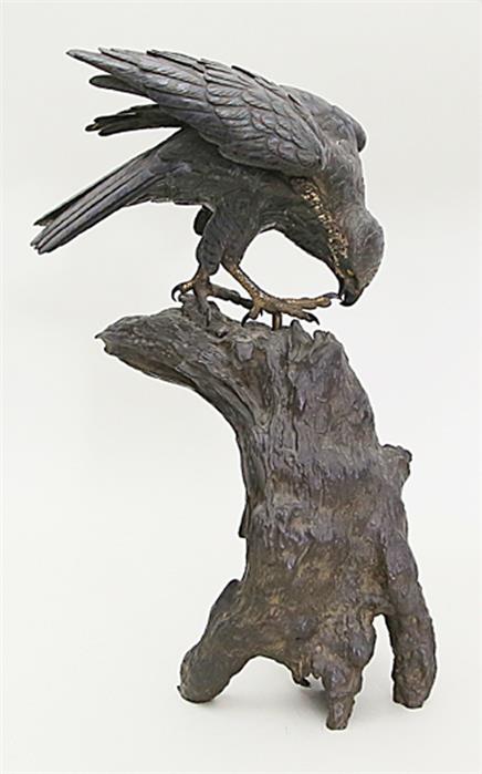 Lebensgroße Skulptur eines Falken auf einem Baumstumpf.