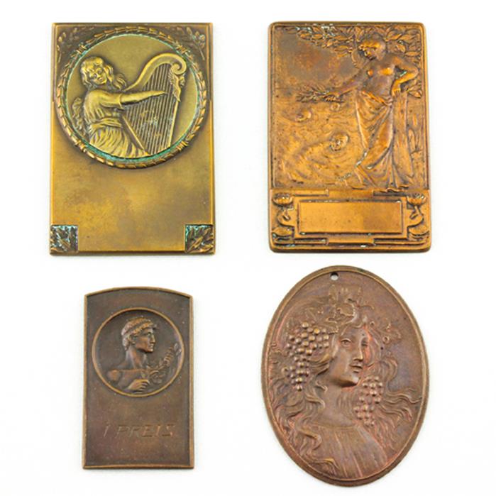 Vier Bronzeplaketten bzw. -medaillen.