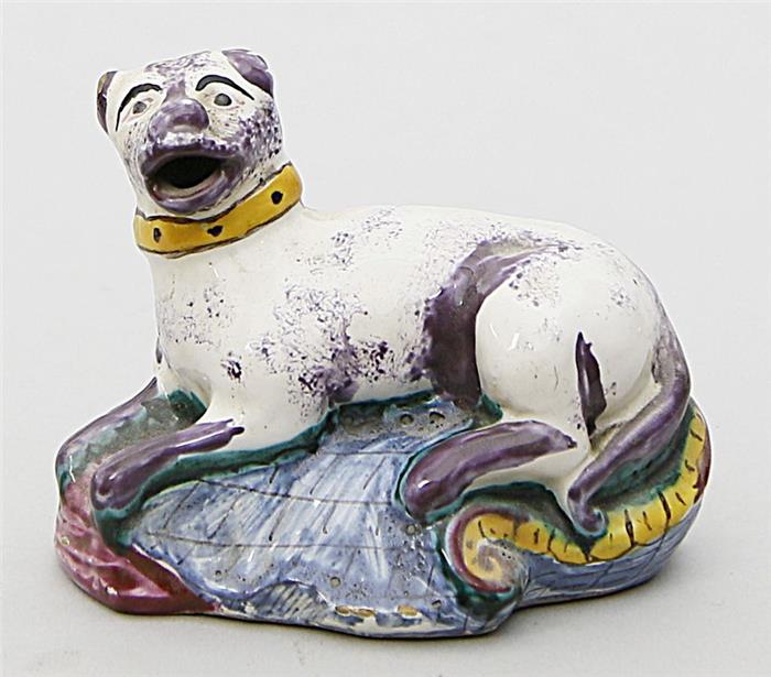 Skulptur eines liegenden Hundes auf Rocaillensockel.